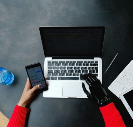 A person using a laptop, smartphone, and tablet with a prosthetic hand, emphasizing digital connectivity.