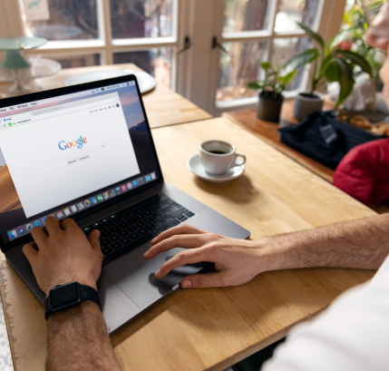 A person uses a laptop for internet browsing. A bright indoor setting with coffee on a wooden table.
