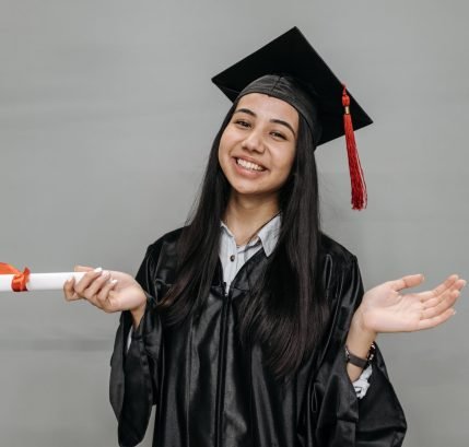 Young woman in graduation gown and cap, smiling and holding diploma. Studio portrait capturing academic success.